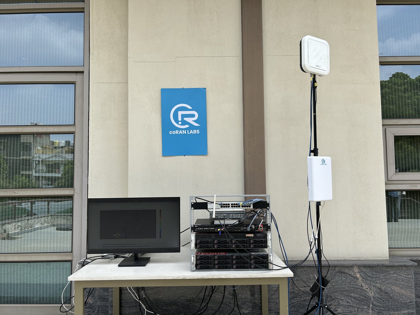 ISAC testbed deployed: coRAN LABS panel antenna on the mast beside the LiteON radio unit and the server rack